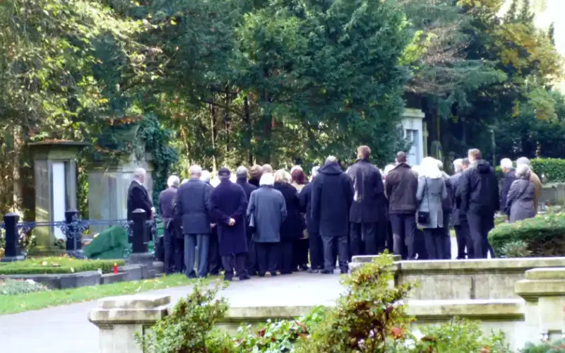 Eine Gruppe von Trauernden steht an einem Grab